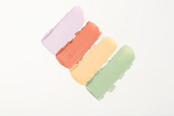 Samples of different color correcting concealers on white background, top view
