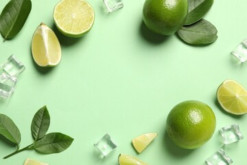 Frame made of ripe limes with leaves and ice cubes on light green background, flat lay