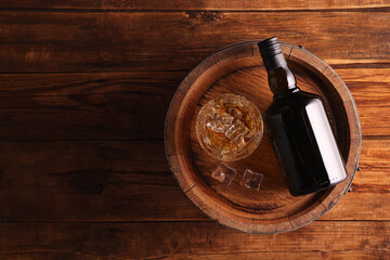 Whiskey with ice cubes in glass, bottle and barrel on wooden table, top view. Space for text