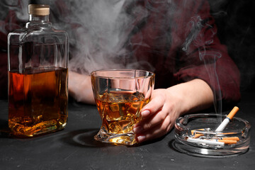 Alcohol addiction. Woman with whiskey and smoldering cigarettes at dark textured table, closeup