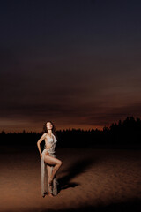 Beautiful Woman posing in a rope swimsuit on the beach among the sand at sunset.