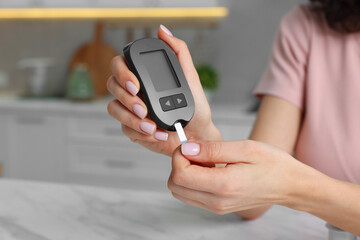 Diabetes. Woman checking blood sugar level with glucometer at marble table in kitchen, closeup. Space for text