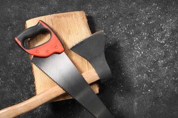 Saw with colorful handle, axe and log on dark gray textured background, top view. Space for text