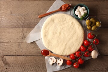 Pizza dough and products on wooden table, flat lay. Space for text