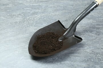Metal shovel with fertile soil on gray textured surface