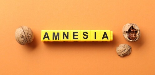 Word Amnesia made of yellow cubes and walnuts on orange background, flat lay
