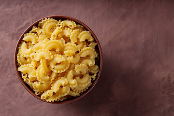Dry Uncooked Creste di Gallo Pasta in Clay Bowl on Brown Background, Copy Space