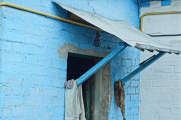 old wooden small primitive wooden canopy with iron gray roof over open doors and blue painted house wall during daytime outdoors