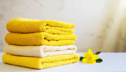 Stack of folded yellow towels on table, light wall on background. Home laundry. Housekeeping concept