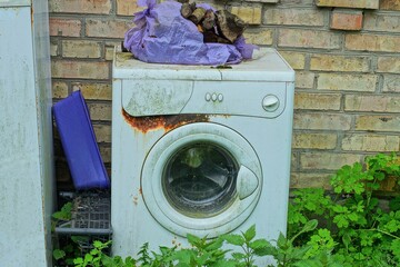 one white old  iron rusty broken closed electric modern discarded washing machine stands on the...