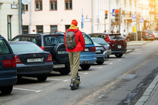 Minsk, Belarus. Apr 13, 2024. Man rides rent scooter along roadway next to parked cars, violating traffic rules. Man on motor scooter rides on city road. Trendy man with Nitro DAYPACKER backpack