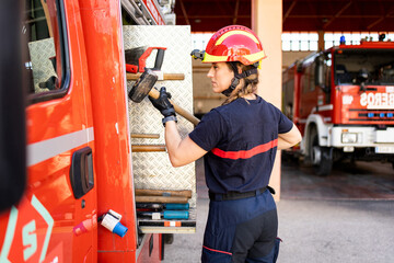 A senior Caucasian woman works as a firefighter dressed in a uniform.The adult woman is pulling a hammer from the side of the fire truck.Concept of women in risky professions.