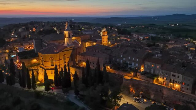 Aerial evening shot of Pienza town in Tuscany, Italy. Church and old houses with city lights, red sunset at background in Pienza