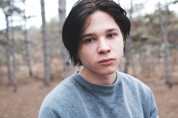 Sad teenage boy 15-16 year old with dark hair in woods outdoor. Looking at camera.