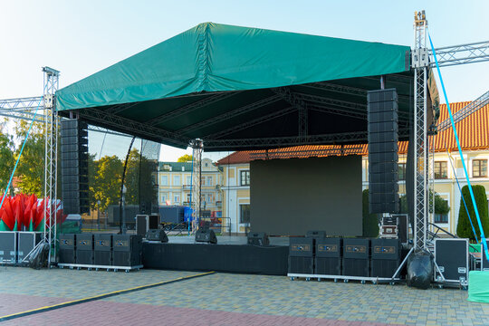 Large indoor outdoor stage for concerts. Professional sound and lighting equipment on stage. Monitor speakers  and big screen on stage.