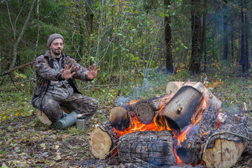 A man warms himself by a fire in the forest.
