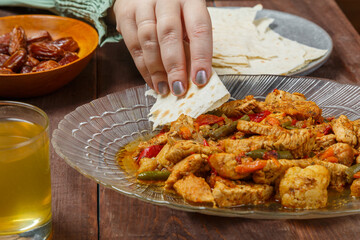 A Muslim woman's hand at the table takes lamb during Ramadan iftar