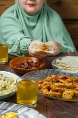 A young Muslim woman in a light khimar at the table takes a flatbread with her hand during Ramadan iftar