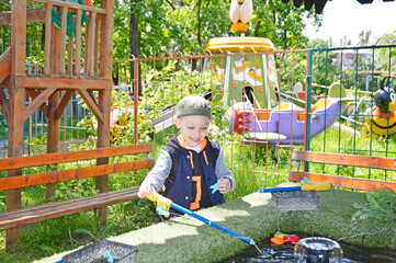 cheerful boy catches fish with a toy fishing rod. attraction with fishing in the recreation area of...