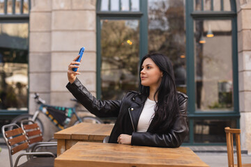 Happy woman using smartphone at cafe. Smiling brunette woman using smart phone make selfie, spends...