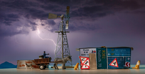 A rural scene from South Africa created with miniature items.  A shack made of Nothern Cape, South Africa, road signs next to a donkey cart, with a windmill and dam in the background.