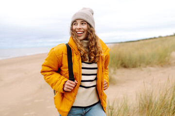 Happy woman in a yellow coat walks along the seashore.  Travel, tourism concept. Active lifestyle.