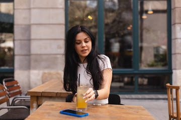 Close-up of young caucasian woman enjoying drinking orange lemonade sitting in cafe. Brunette in...