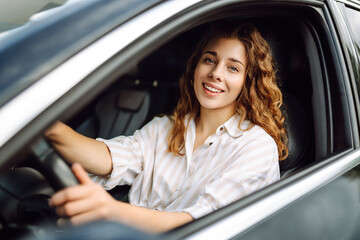 Young smiling woman driving a car drives around the city. Car travel, lifestyle, carshering concept.