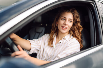 Young smiling woman driving a car drives around the city. Car travel, lifestyle, carshering concept.