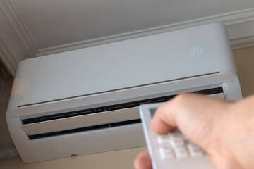 Man's hand with a remote control turns on the air conditioner to heat the room. Electric heating of...