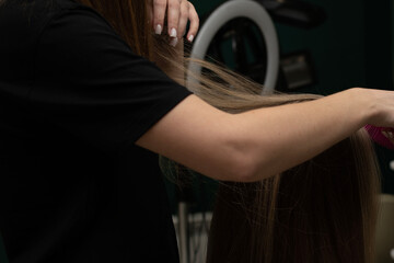 Beauty sphere. The master hairdresser does styling and combing the hair. Combs a client's long hair...