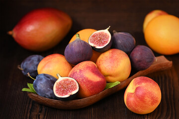 still life with fruit on a wooden background, nectarines, plums, figs, orange, mango