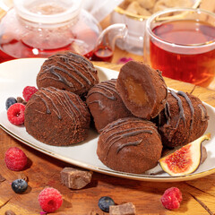 Warm homemade chocolade  sponge cake served on parchment paper, accompanied by fresh berries and cup of tea, set on rustic wooden table. Concept of home comfort and delightful afternoon treats