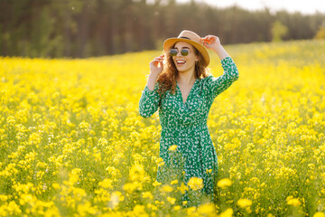 Naklejka na ściany i meble Beautiful woman in bright dress in rapeseed field. Nature, vacation, relax and lifestyle. Summer landscape.