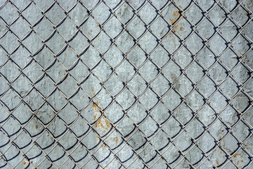 Fragment of an iron mesh with square cells against the background of a wall covered with peeling gray paint with rust, for use as an abstract background and textures.