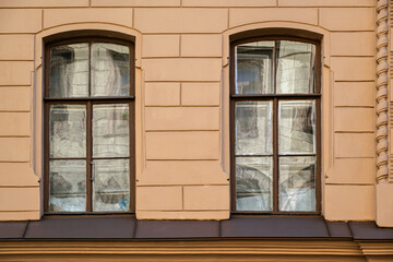 Two rectangular windows with old brown wooden frames with reflections on the glass, against a beige...