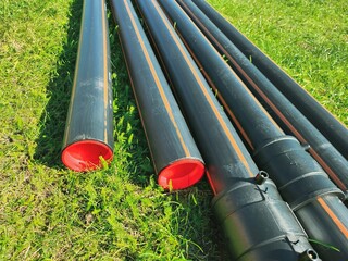 An assortment of black plastic pipes of varying diameters arranged on lush green grass, creating an...