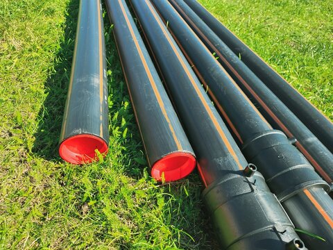 An assortment of black plastic pipes of varying diameters arranged on lush green grass, creating an industrial scene against a vivid green backdrop, harmonizing utility with nature