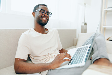 Smiling African American Freelancer Working on Laptop on Sofa in Modern Home Office with Cyberspace...