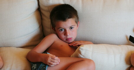 Small boy watching movie seated on sofa at home