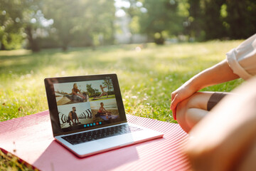 Online fitness classes. Young woman practicing yoga in front of laptop, watching online tutorials in the park. Online training, course.