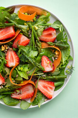 Spring light salad with strawberries, asparagus, carrots, arugula leaves, spinach and flax seeds, nuts and olive oil dressing. Light salads with fruits and berries, sweet and salty taste, close up