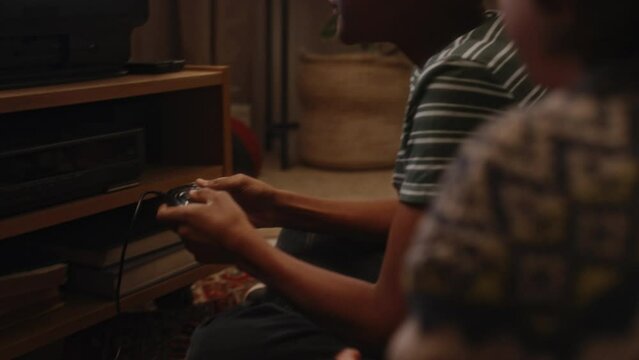 Over shoulder handheld footage of African American gen Y boy winning TV console video game and giving high five to unidentified friend at home, atmospheric childhood in 90s