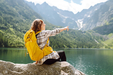 Happy tourist woman  enjoys the view of the mountain lake in sunny weather. Scenery of the majestic...