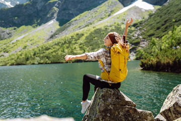 Happy tourist woman  enjoys the view of the mountain lake in sunny weather. Scenery of the majestic...