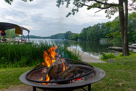 Campfire on the shore with docks, pontoon boat, and lake in the background.