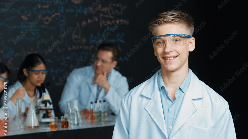 Poster smart student looking at camera while diverse group doing experiment. attractive academic boy standi