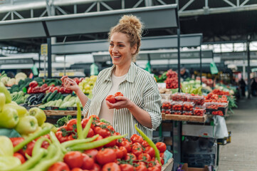 Smiling woman with basket buying fresh tomato at food market.