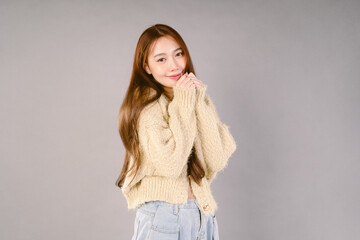Beautiful young Asian woman in warm knitted green sweater standing, warm winter cold season fashion accessories trend, posing and looking at camera on gray studio background isolated.
