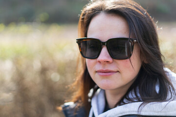 The young girl wearing sunscreen glasses smiles in her jacket and sweater on the street